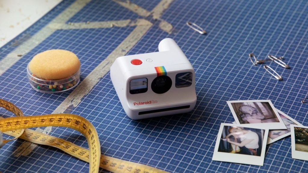 Polaroid Go camera sitting diminutively on a cutting mat, next to scattered sewing supplies and Polaroid Go pictures.